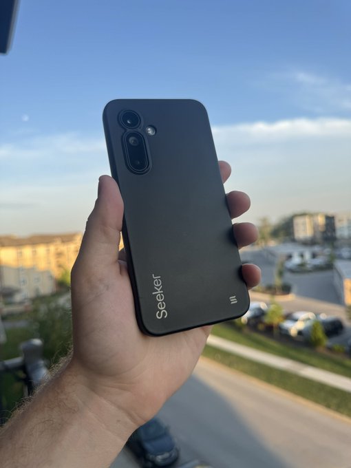 A hand holds up a sleek black smartphone branded with "Seeker" on the back, set against a scenic rooftop view, symbolizing pride in ownership as the post celebrates $SKR's 75% surge in 24 hours and rallying fellow holders.
