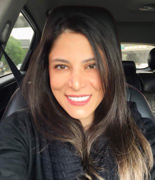 A selfie of a smiling woman with long dark hair sitting inside a car.