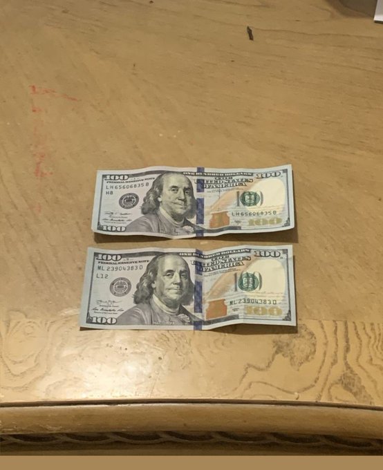 Two creased $100 bills displaying Benjamin Franklin are laid on a wooden table. The visible serial numbers read "LH6500635 B" and "ML23904383 D." The post's question about grinding for the money pairs with the image to suggest the hard work required to earn such bills.