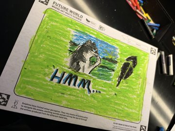 A handwritten message reading "HMM..." on a green-bordered activity card from the Art Science Museum's Future World exhibit in Singapore, displayed on a table with crayons visible nearby. The handwritten note reflects the $HMM ticker shown on the card, connecting to the post about the token making its mark on the museum's interactive exhibit walls.