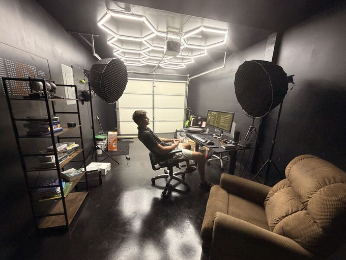 A person sits at a computer setup in a dimly lit room with distinctive hexagonal LED ceiling lights, surrounded by professional photography softboxes, shelving, and a brown couch, reflecting a tech-savvy workspace lifestyle that parallels the post's narrative of early Bitcoin mining and a trade-for-services arrangement at a startup.
