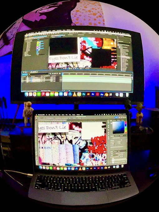 A dual-monitor video editing setup displays the title 'Eyes Don't Lie' on both the desktop monitor and a laptop, with small figurines sitting on the desk and a fisheye lens effect applied to the photo.