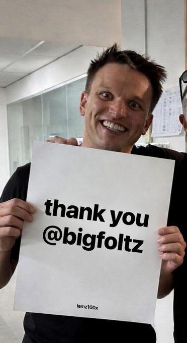 A smiling man holding a sign that reads 'thank you @bigfoltz' with 'lemz100x' printed at the bottom.
