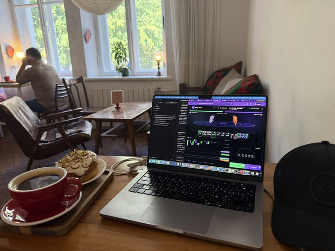 A laptop on a wooden café table displays a video editing timeline with "0.000%" visible on screen, accompanied by a cappuccino and pastry on a tray. In the background, a man sits alone in a cozy post-Soviet style café, fitting the "solo leveling" theme suggested by the caption.