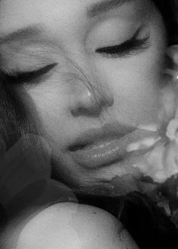 A black-and-white close-up of a woman with closed eyes and slightly parted lips, her face partially obscured by what appears to be petals, capturing an intimate, dreamy aesthetic that complements the melancholic tone of the song "Petal" by Ariana Grande.