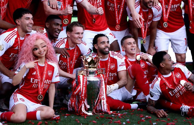 A group of soccer players, dressed in red and white uniforms with gold accents, celebrate their victory on a lush green field, holding trophies and medals.