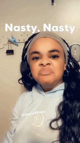 The image features a person with long black hair wearing a grey headband, posing for a picture against a white background. The caption of the image reads "Nasty, Nasty", which seems to be a reference or joke about the current situation. The person's face is turned towards the camera, and they appear to be making a funny or ironic facial expression.
