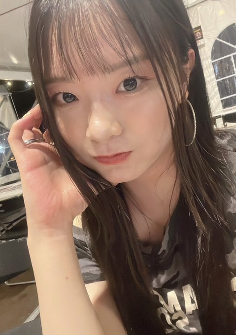 A close-up selfie of a young woman with long dark hair, bangs, and blue eyes posing in what appears to be a salon.