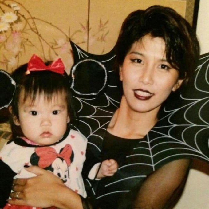 A woman holds a baby wearing a Minnie Mouse outfit with a red bow, posing together in a Halloween-themed setting with spiderweb backdrop. The "#Mina" caption likely refers to the child's name or a sweet nickname for the adorable little girl dressed as Disney's iconic Minnie Mouse.