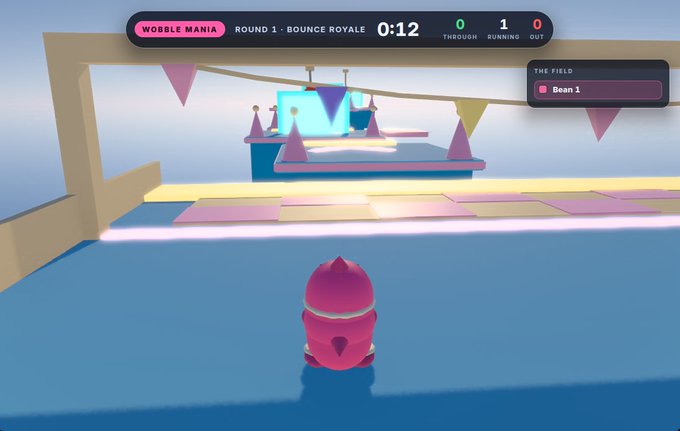 A screenshot from the video game 'Wobble Mania' showing Round 1 - Bounce Royale, with a timer at 0:12, scores of 0 Through and 1 Running, and a pink character facing an obstacle course with cones and bunting.