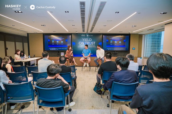 A panel discussion titled "Yield on Trust" hosted by HashKey Cloud and Cactus Custody takes place in a modern conference room, with three speakers seated on stools facing an audience of attentive attendees. The event banner and accompanying post emphasize the theme of holding and actively using Bitcoin, aligning with the engaged dialogue captured in the image.