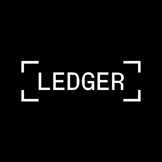 The image displays the Ledger logo in white text on a black background, framed by corner brackets. The logo ties directly to the post about Ledger's new AI Agent Stack, representing the crypto hardware wallet company enabling AI agents to interact with users' crypto wallets while maintaining security through hardware-based transaction approval.