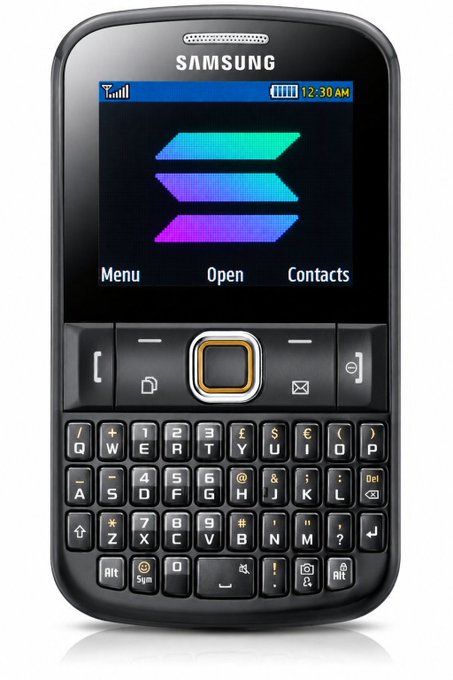A black Samsung mobile phone with a physical QWERTY keyboard is displayed, featuring a screen showing a colorful logo and the time 12:30 AM.