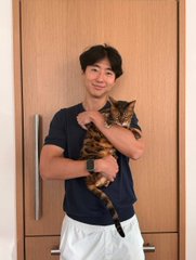 A man in a navy polo shirt and white shorts smiles while holding a brown tabby cat indoors. The image accompanies a post celebrating a full-circle moment featuring "$KIRA" and mentions "@kiraoninjective" as the "CTO of @injective," suggesting the cat pictured is Kira.