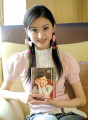 A young woman with pigtails wearing a pink top holds a photo card showing a man, sitting against a striped background.