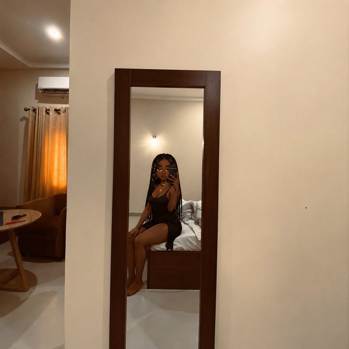 A mirror selfie of a woman in a black dress taking a photo with her phone in a bedroom, with a curtain and living area visible to the left.