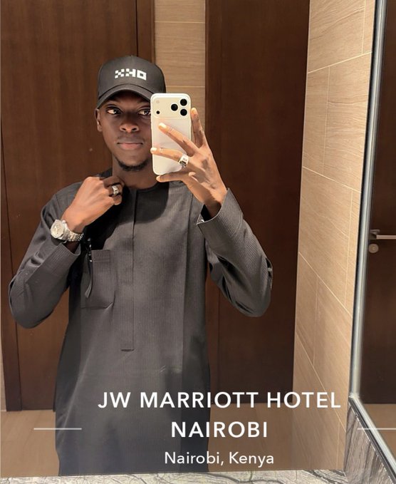 A mirror selfie of a man wearing a black cap and traditional gray attire at the JW Marriott Hotel in Nairobi, Kenya.