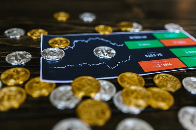 The image features a blackboard with a graph of cryptocurrency prices, including Bitcoin and other coins like Dogecoin. The graph shows that Bitcoin has been rising over time while other coins have been falling. The text in the image suggests that there is an ongoing discussion about investing in cryptocurrency, specifically Bitcoin, as it seems to be performing well compared to other coins.