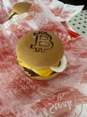 A burger branded with the Bitcoin "₿" logo sits on branded Steak 'n Shake wrapper paper, humorously illustrating the poster's claim of paying 33,480 sats (a fraction of a Bitcoin) for two burger meals at Steak 'n Shake.