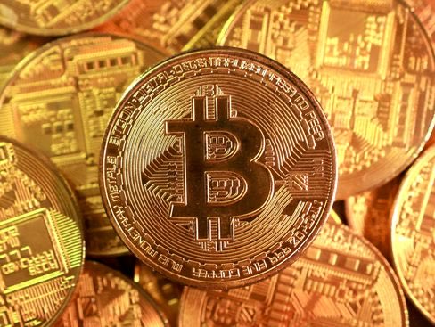 Close-up of golden Bitcoin coins stacked together, with the prominent '₿' symbol and 'BITCOIN DIGITAL DECENTRALIZED PEER TO PEER' text visible around the edge of the central coin.