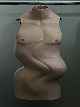 A bare male dressmaker's mannequin torso hanging on a rack against a gray background.