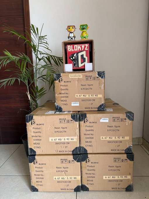 Stacked cardboard boxes of 'BLOKYZ' brand resin figures, with two small figurines displayed on top.