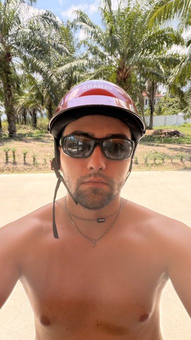 A shirtless man wearing a red "SHAMAN" helmet and sunglasses takes a selfie in front of palm trees, with the post playfully asking followers to drop their $SOL (Solana) crypto wallet addresses in a "good morning" greeting. The casual, tropical vibe of the image complements the laid-back crypto community engagement, with the helmet's text tying into a Shaman-themed persona common in the Solana/NFT space.
