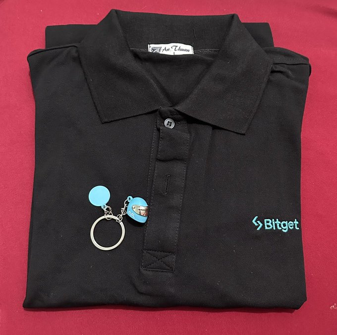A folded black polo shirt branded with the "Bitget" logo in teal on the chest is displayed on a red background, accompanied by a Bitget-branded blue keychain, representing one of the web3 prize gifts mentioned in the post.