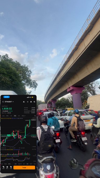 A traffic jam of motorcyclists and cars waits under an elevated roadway, with a phone screen overlay showing the ETH/USDT trading pair at 1,928.32 (+1.85%).