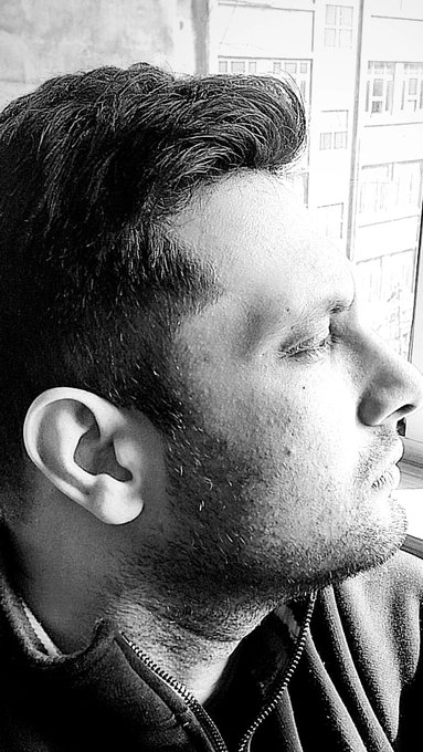 A black and white close-up profile photo of a bearded young man looking out a window, with his eyes closed.