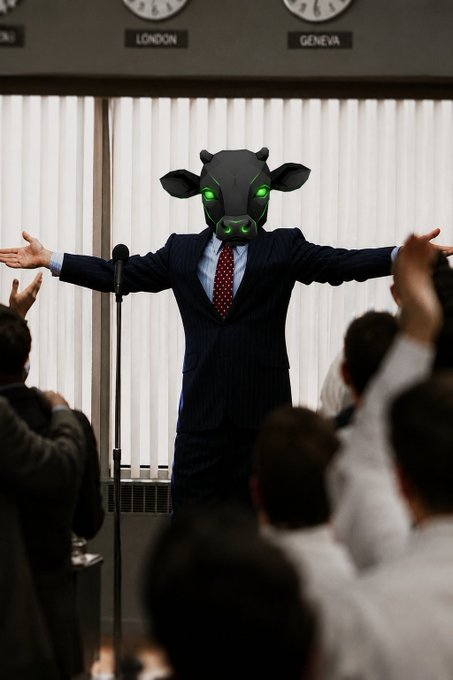 A figure in a dark suit with a red tie and a bull mask with glowing green eyes stands with arms outstretched before an applauding audience, beneath clocks labeled "LONDON" and "GENEVA." The bull mask symbolizes a bullish market rally, mirroring the post's celebration of $ANSEM and $BABYANSEM's strong price performance.