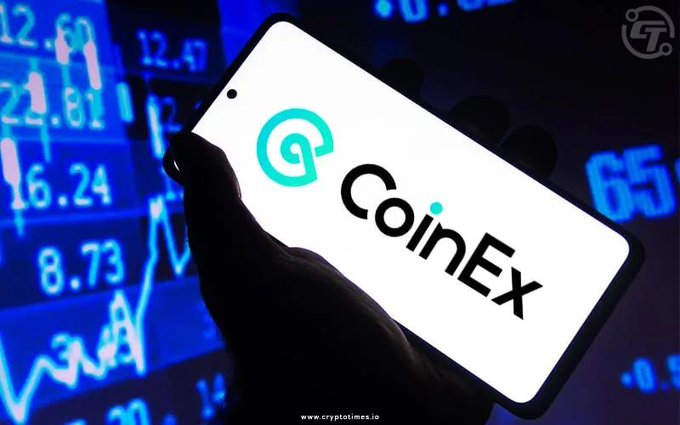 A close-up photograph of a hand holding a smartphone displaying the CoinEx cryptocurrency exchange logo against a backdrop of blue financial market charts.