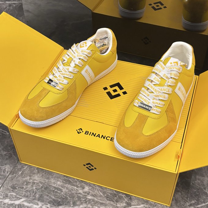 A pair of yellow sneakers with "BINANCE" printed on the laces rests atop a matching yellow Binance-branded shoebox, displayed on a marble floor as a Mid-Autumn Festival gift from Binance. The image visually represents the caption's celebration of receiving the branded footwear, symbolizing the user's well wishes for Binance's trading volume and growth.