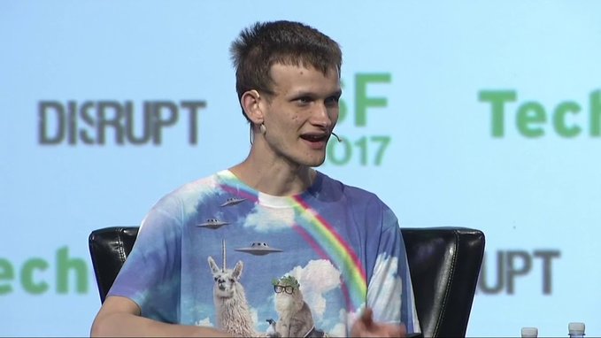 Vitalik Buterin speaking at TechCrunch Disrupt SF 2017, wearing a colorful t-shirt featuring a llama, UFO, and rainbow design.