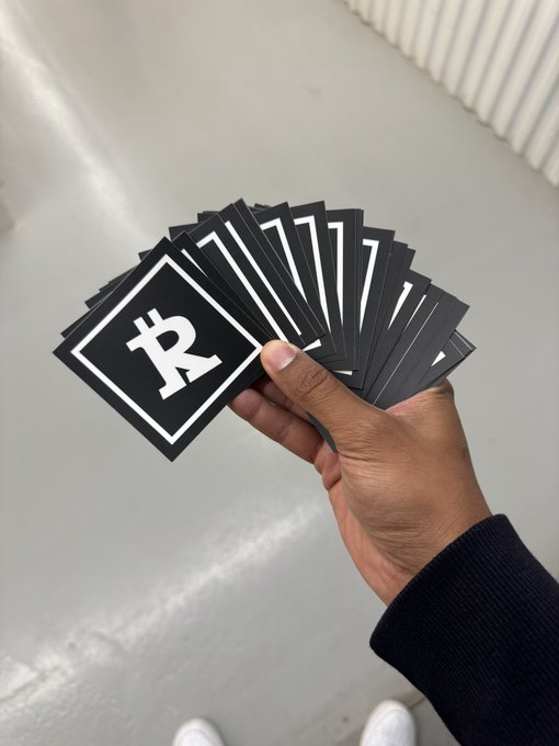 A hand holding a fan of black cards, with the top card displaying a white Bitcoin 'B' symbol.