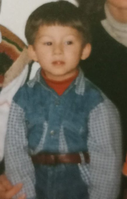 A vintage photograph of a young Asian boy wearing a blue and white checkered denim outfit over a red turtleneck with a brown belt.
