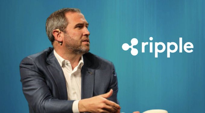 The image shows Ripple CEO Brad Garlinghouse speaking on stage, with the Ripple logo displayed on a blue backdrop behind him. This visual accompanies news of his recent indication that Ripple may consider pursuing an IPO following the resolution of its SEC legal battle.