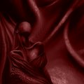 A dark, moody abstract image in deep red tones, featuring shadowy draped fabric and a small spherical form in the foreground.