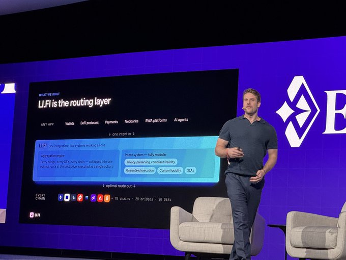 The image shows a man standing behind a large screen displaying information about the routing layer, with his hands outstretched as if he's presenting or explaining something related to the topic. The background features a blue wall with a white logo for "B" Bank of America.