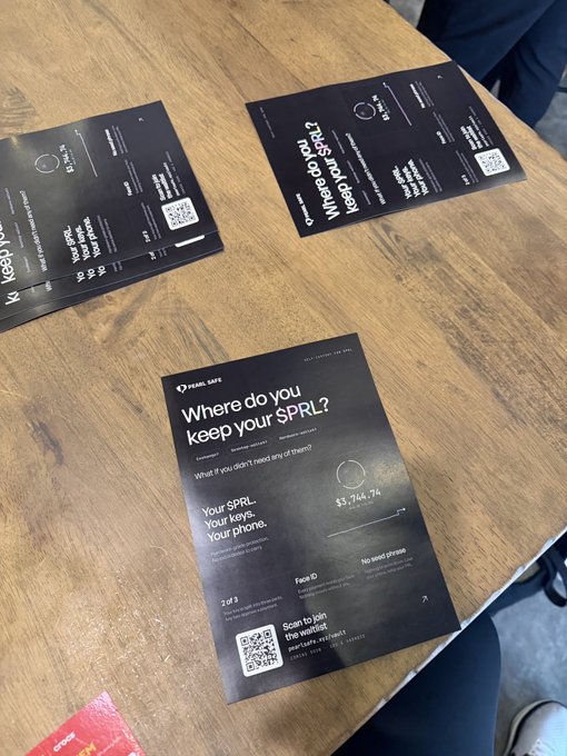 Black informational flyers on a wooden table reading 'Where do you keep your SPRL?' from Pearl Safe, explaining how to secure cryptocurrency on a phone.