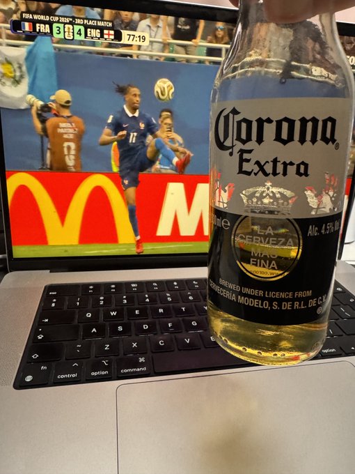 A Corona Extra beer bottle held in front of a laptop showing the FIFA World Cup 2018 third place match between France (FRA 3) and England (ENG 4) at 77:19, with a McDonald's logo visible in the background.