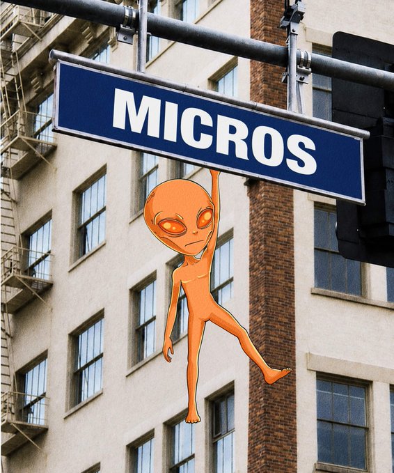 A digitally edited image of a street sign reading "MICROS" (instead of MICROS way) being held up by an illustrated orange alien in front of a brick building.
