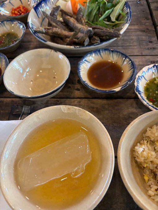 A table spread of Vietnamese cuisine featuring fried fish with herbs, various dipping sauces (including fish sauce and chili), a bowl of clear broth, and a bowl of rice.
