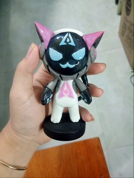 A hand holds a small handmade figurine of a black and white cat mascot with pink horns and a glowing cyan "A" symbol on its forehead, designed as the GenLayer mascot. The post highlights the creator's reflection on how blockchains excel at clear rules but struggle with nuanced, context-dependent decisions—concepts visually represented by the futuristic, AI-themed character.