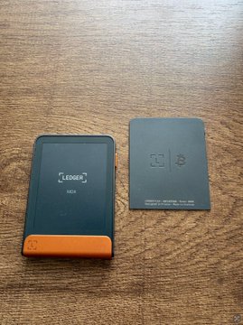 A Ledger Nano cryptocurrency hardware wallet sits on a wooden table next to its product manual/booklet. The image appears to counter the post's claim by showing the wallet and its documentation, visually reinforcing the Ledger brand being criticized.