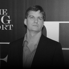 The image shows a man in a dark suit posing at what appears to be a media event, with partially visible text "HE G ORT" in the background that is likely part of "The Big Short" promotional signage. This relates to the post about Michael Burry, the investor famous for predicting the 2008 housing crisis and depicted in "The Big Short," now warning of a potential AI bubble and shifting his trading strategy to put options on companies like Micron ($MU).