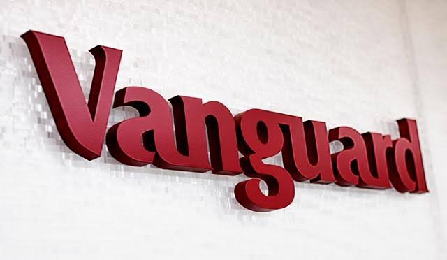 A 3D red sign displays the "Vanguard" logo mounted on a textured white wall, representing the asset management firm mentioned in the post about its new cryptocurrency business leadership position.