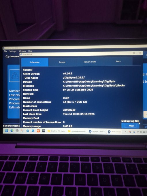 A laptop screen displays the DigiByte Overview application showing client version v9.26.5 and network synchronization details, with the taskbar visible at the bottom.