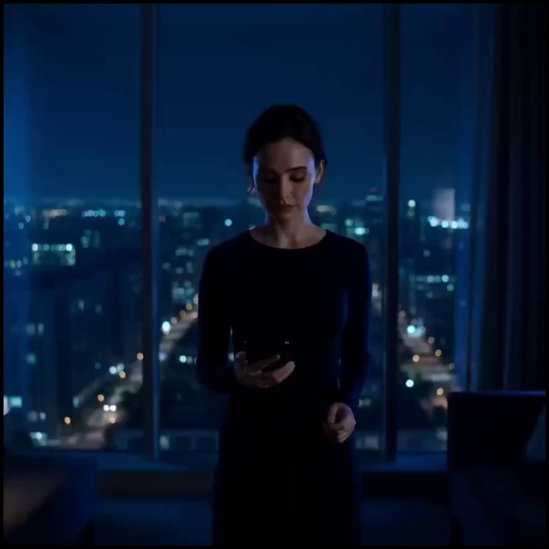 The image shows a woman standing in front of a window, looking down at her phone. She appears to be using an app or browsing through some content on her device. The photo has been edited with a filter that gives it a blue tint, giving it a dreamy and ethereal appearance. The caption below the image provides information about the post's title and the type of reward it offers for completing the task.