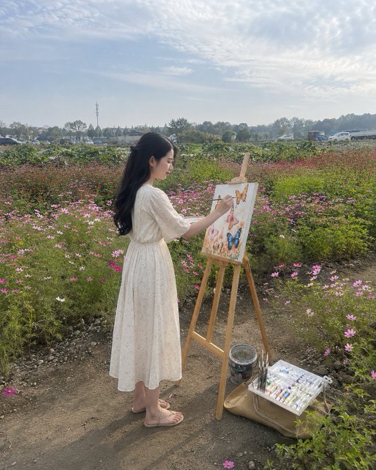 The image features a woman dressed in white, standing next to an easel while painting outdoors. She appears to be focused on her artwork as she creates a beautiful picture. The setting includes a field with flowers surrounding her, adding a serene atmosphere to the scene. In addition to the woman and her art supplies, there are several cars parked nearby, suggesting that this location might be a popular spot for artists or visitors seeking inspiration in nature.

The post is titled "gm gm fam, just scrolled through @quipnetwork press page like an old school news junkie". This indicates that the woman's artwork has caught the attention of others who appreciate her talent and creativity. The image also contains a caption about quantum classical testnet hitting real coverage, which could be related to the art world or simply a random piece of information shared by someone who came across the post.
